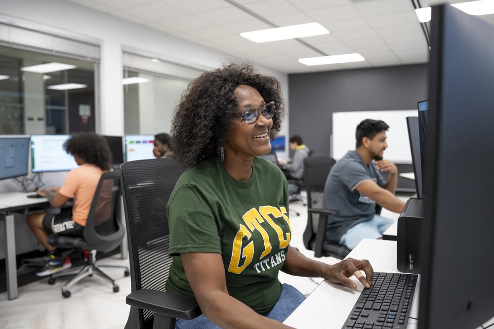 An older African American female student in a GTCC T-shirt sits in front of a computer.