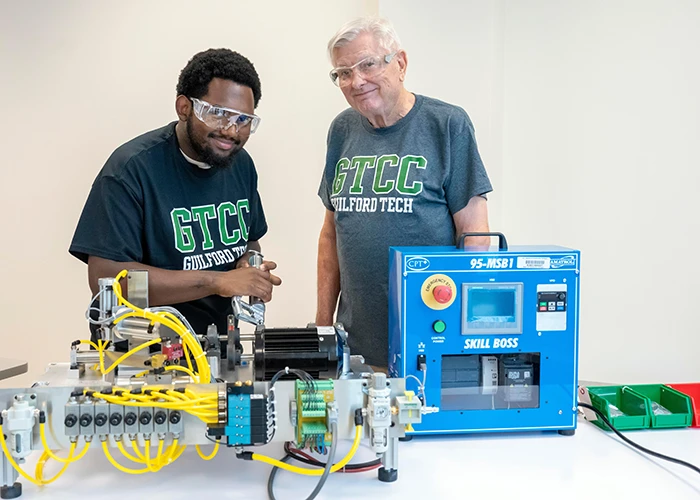 A male student and instructor work a small piece of equipment used in the certified product technician training.