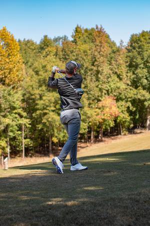 A golf, back to camera, swings with Grandover building in the background.