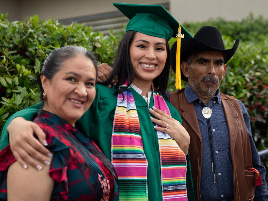 A female graduate, center, her mother, left, and father, right smile after the ceremony.