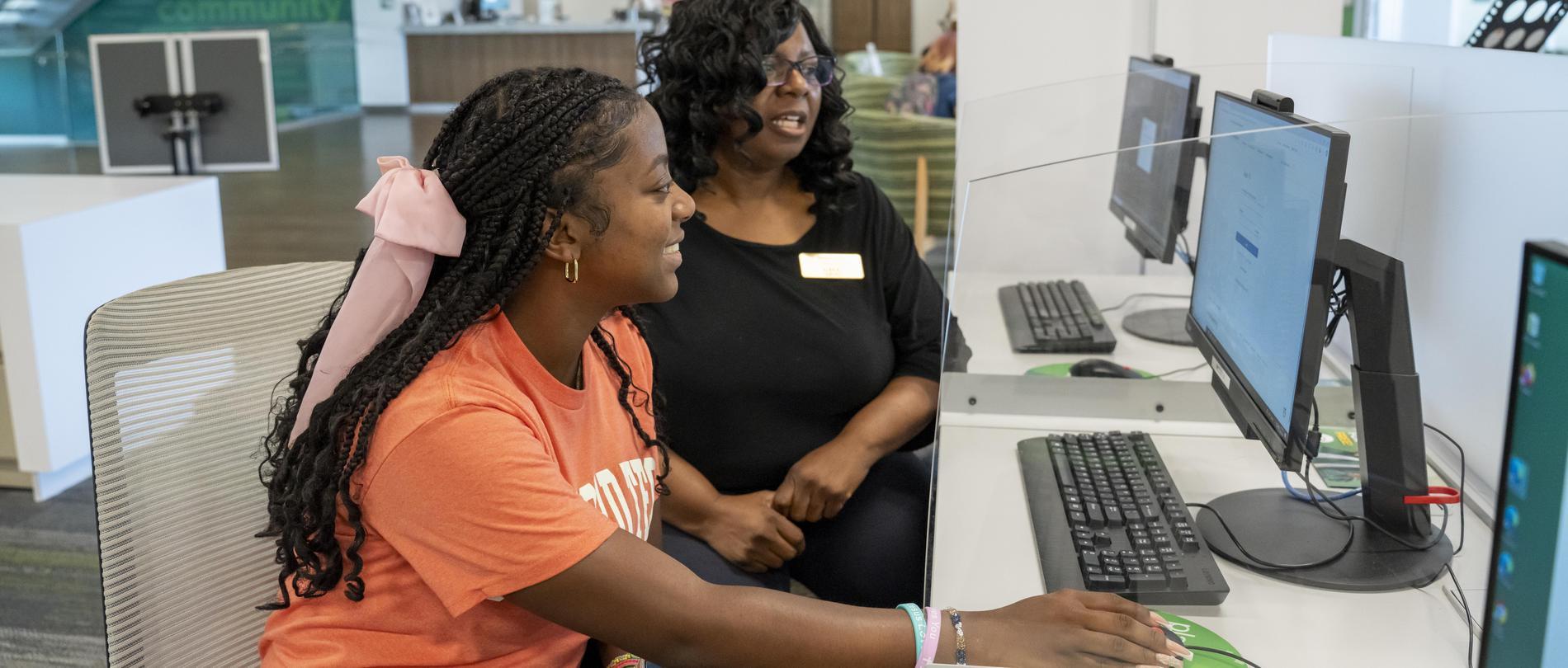 A student and a staff member work at a computer.