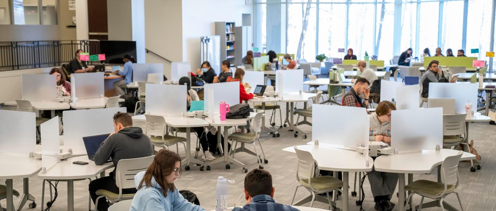 Students studying and working on laptops in the Center for Academic Engagement at GTCC, a bright, open space with collaborative and individual work areas.