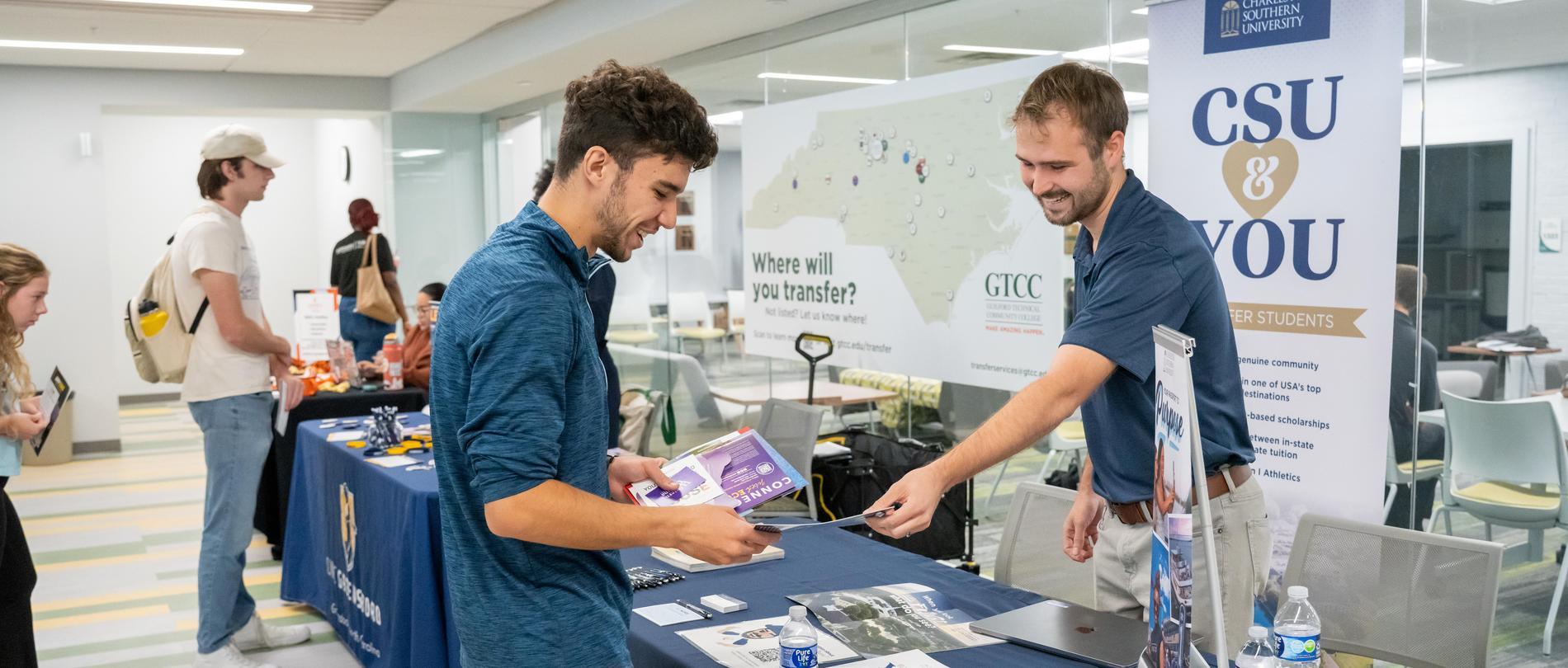 A GTCC student speaks with a university representative at a transfer fair booth, reviewing materials about transfer opportunities.