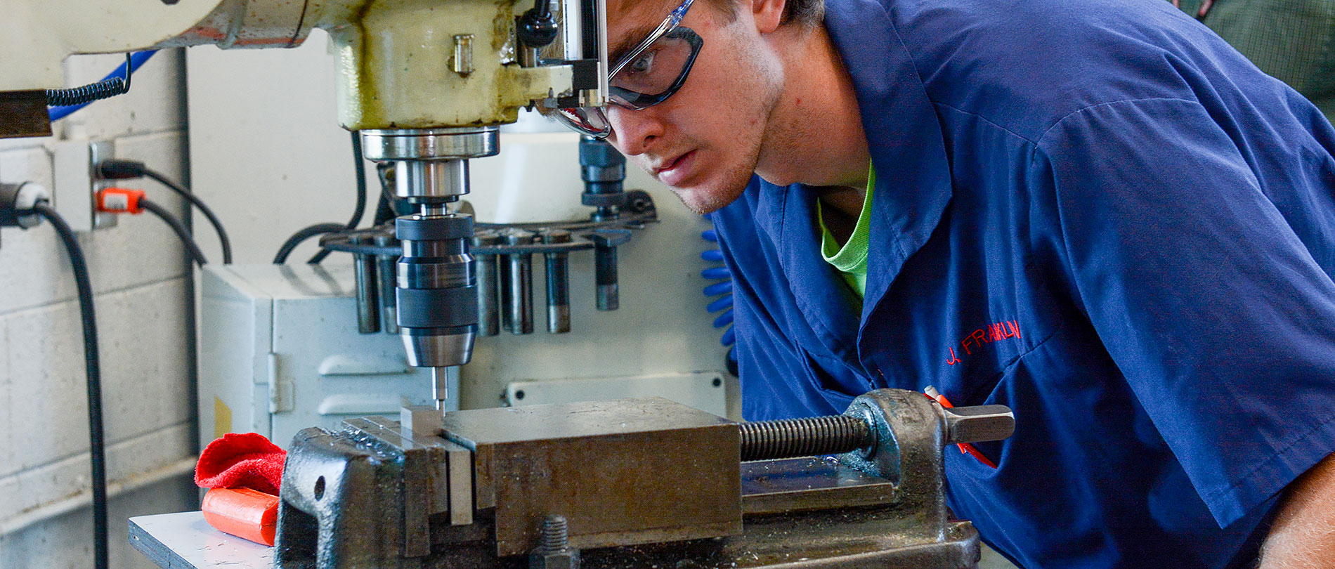 Student intently looks at machining equipment during a class.