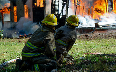Fire fighting students in gear practice putting out a house fire.