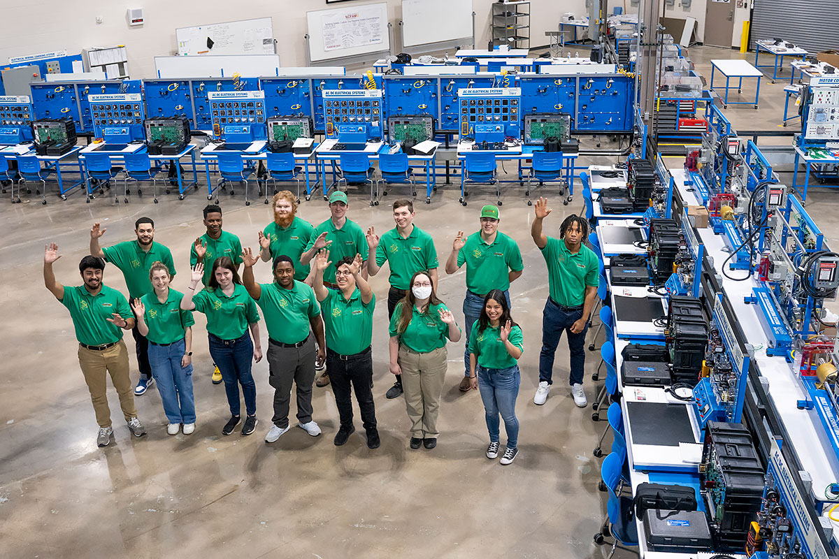 Fourteen members of the FAME Class of 2025 pose for a picture in the training area in the Center for Advanced Manufacturing 