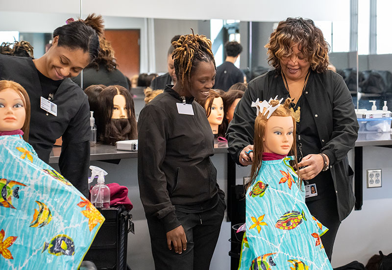 Instructor shows student how to cut hair.