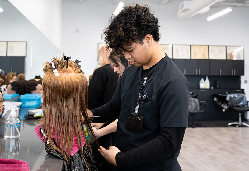 A male student cuts a mannequin's hair.