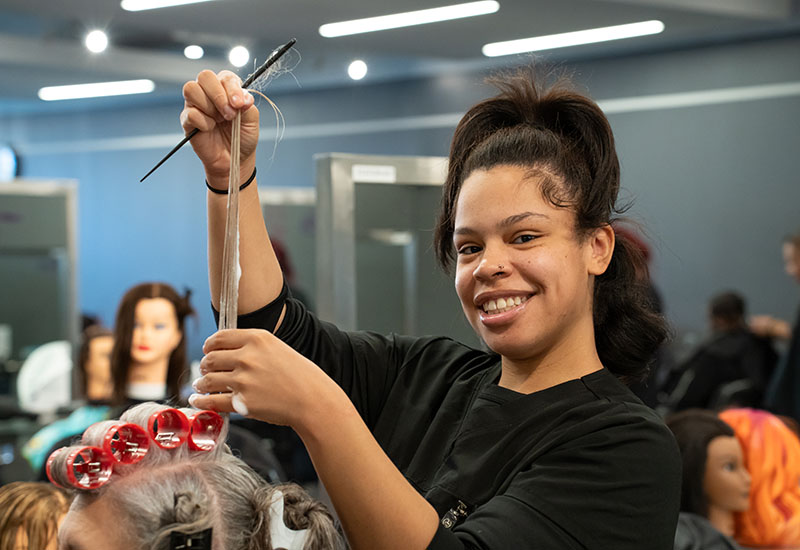 A student cuts a mannequin's hair.