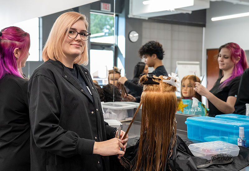 A student cuts a mannequin's hair.