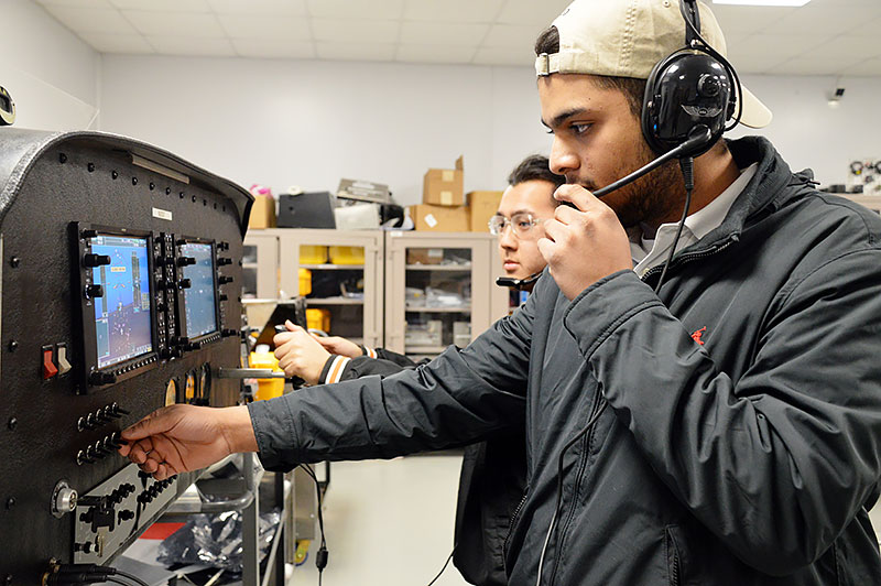 Students check a communications panel in a lab.