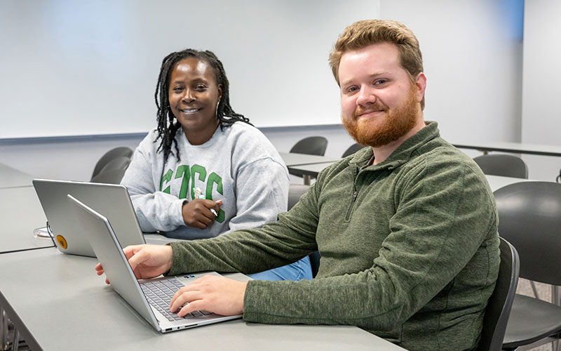 Adullt GTCC male and female students sitting at a classroom desk smiling at the camera