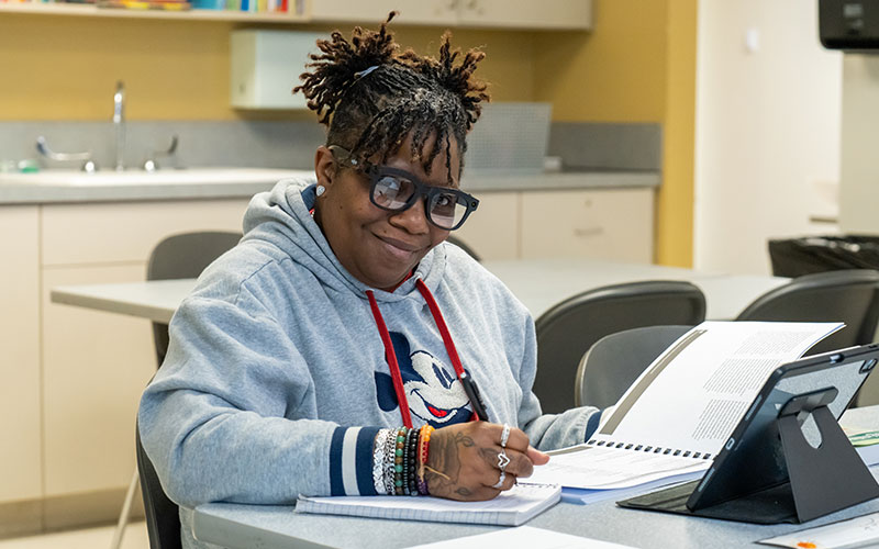 Adult GTCC student sitting at classroom desk writing in notebook and smiling