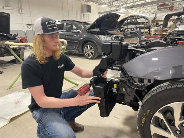  Jadon Layton kneels while working on the front end of a car.