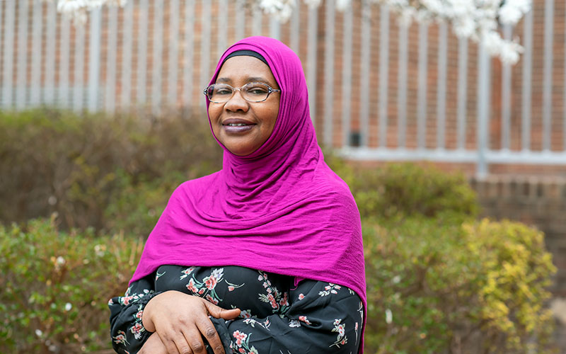 Fati Seyni, head covered with a pink scarf, stands in a garden setting.