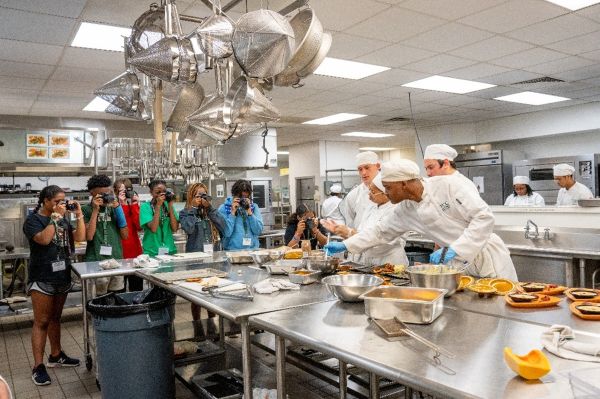 Participants in the cooking camp watch as a chef shows them how to prepare a meal.