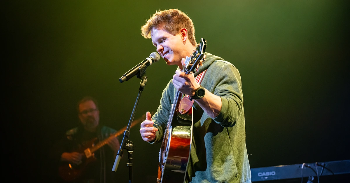 A male student plays a guitar and signs into a mic on stage.