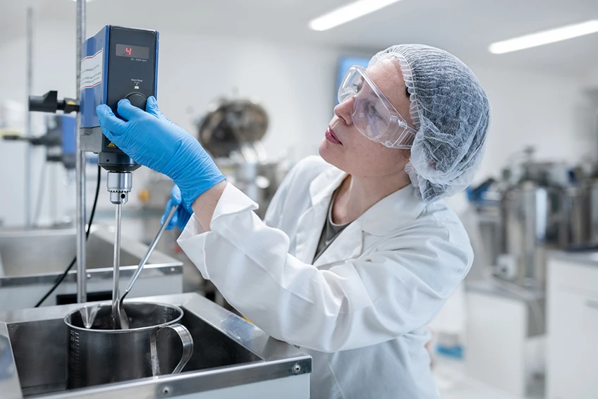 A female worker at a processing plant uses a mixer  while wearing personal protective equipment.
