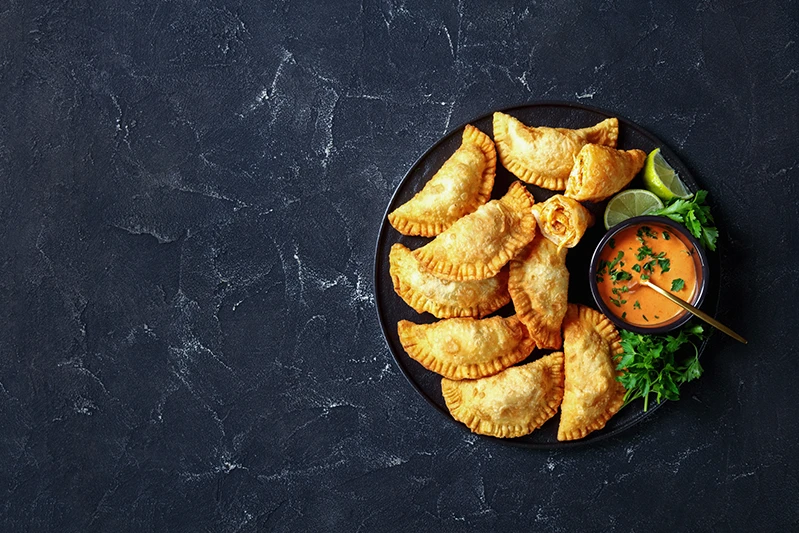 Deep fried Buffalo Chicken Empanadas with Low Calorie Dip on a black platter on a concrete table.