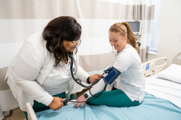 Female nursing student checking blood pressure of female patient